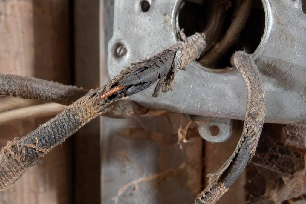 Frayed fabric jacket and cracked rubber insulation exposing bare copper at a metal junction box in an older home.