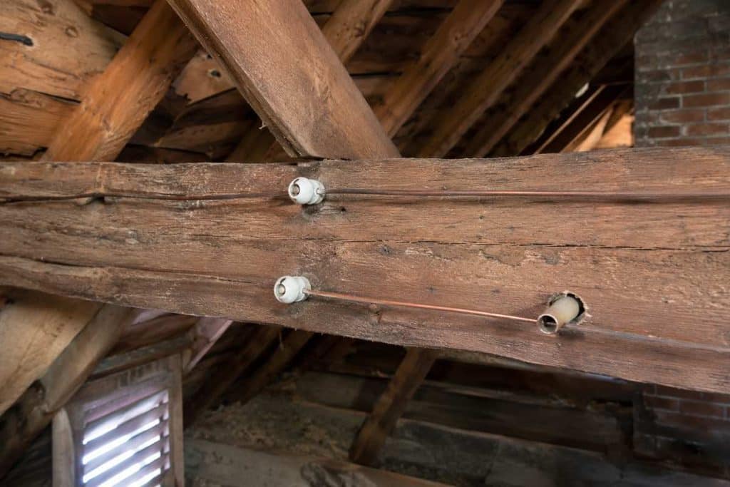Single copper conductors on ceramic knobs and through a ceramic tube on attic framing, hot and neutral spaced apart.